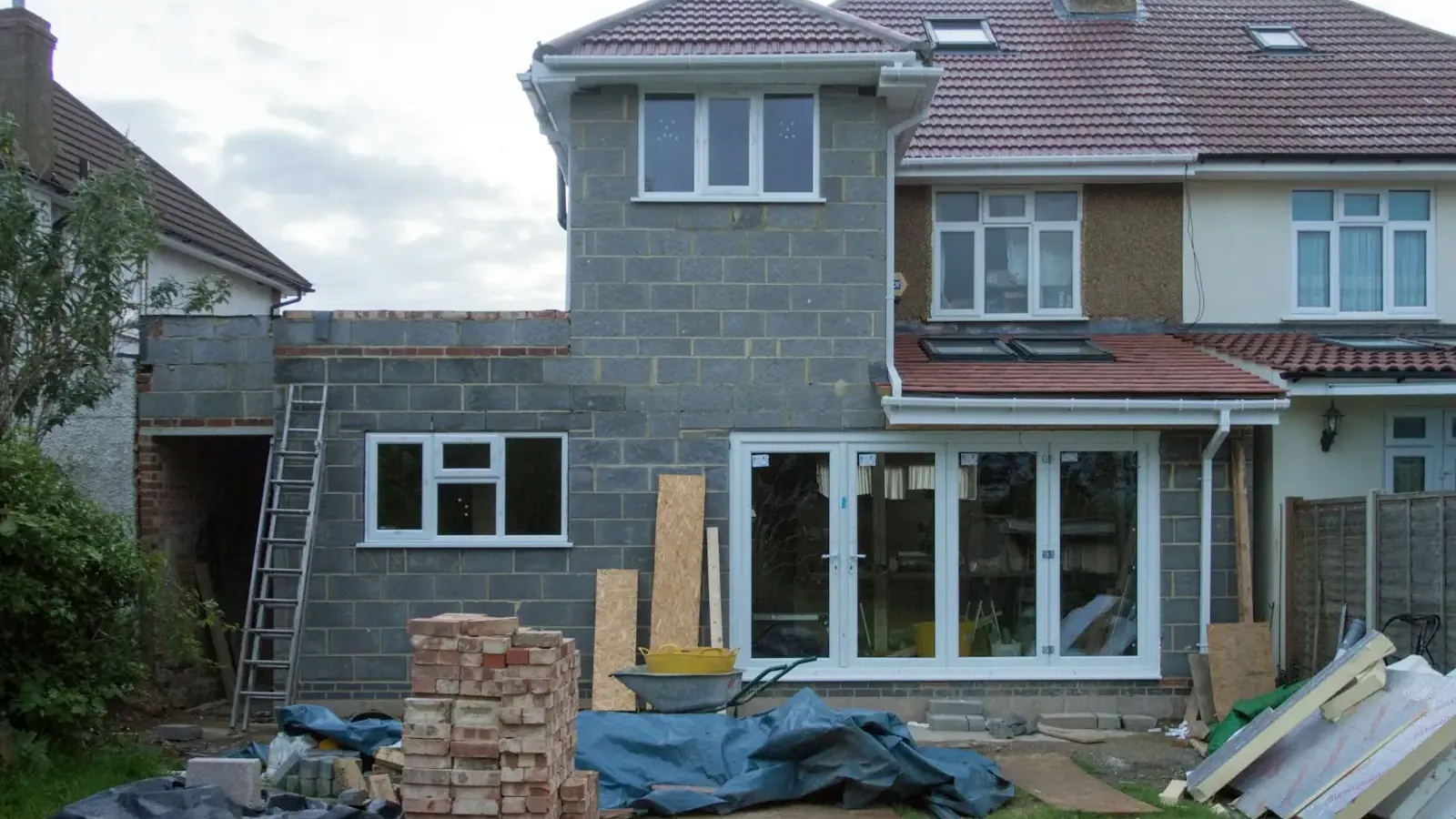Two-storey rear extension in blockwork on a semi-detached house, with bricks and materials stacked in the garden