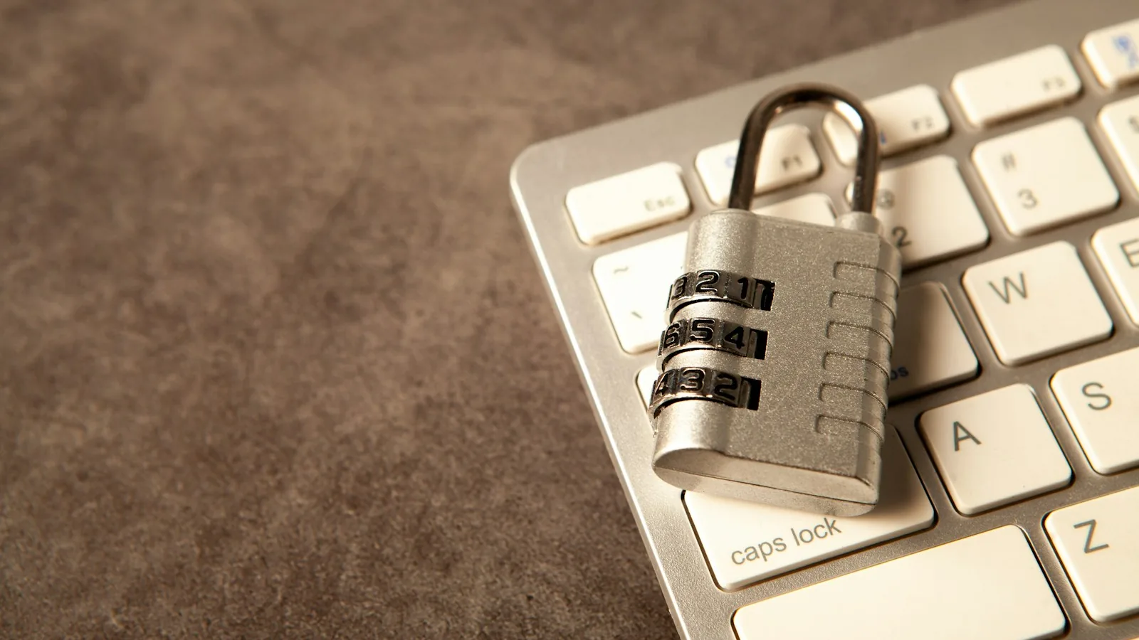 A silver combination padlock resting on a white laptop keyboard beside the caps lock key