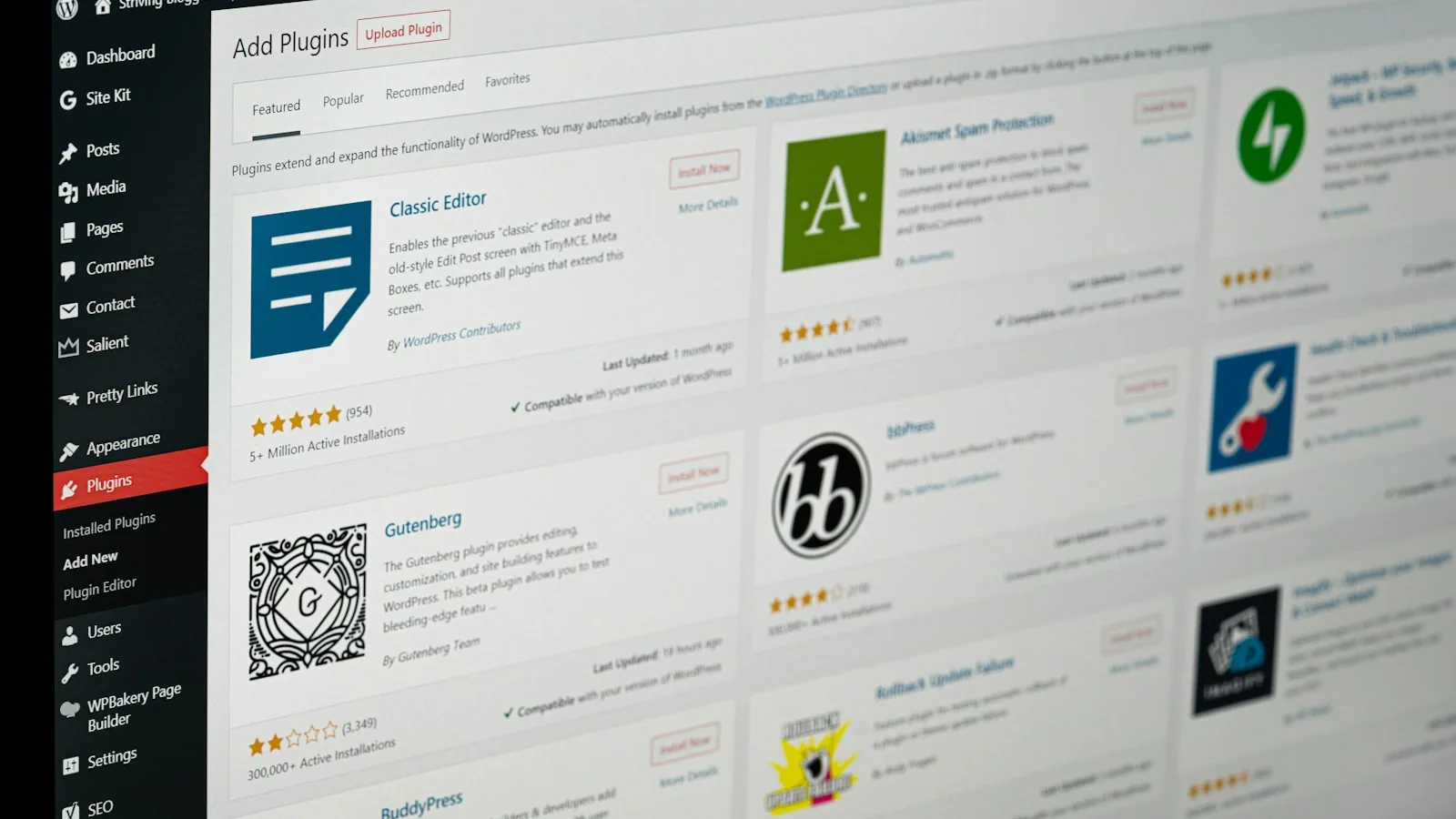 The WordPress Add Plugins screen on a monitor, showing plugins available to install with their ratings