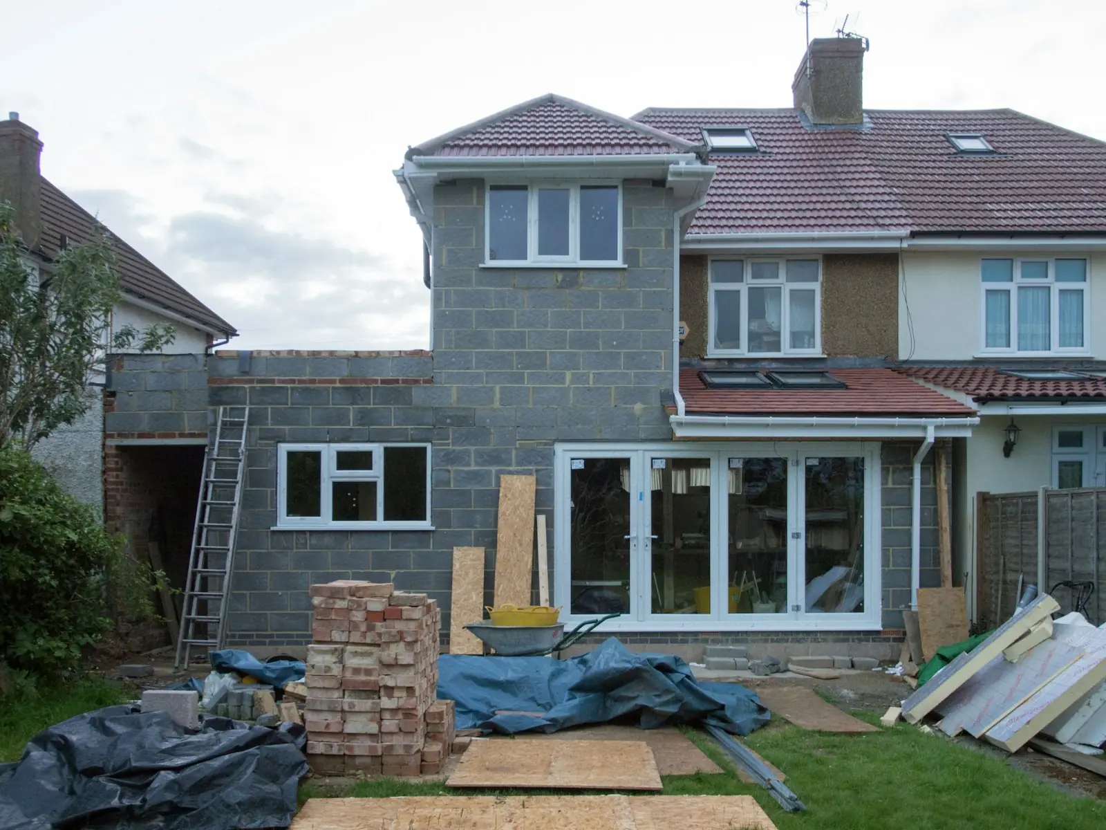 Two-storey rear extension in blockwork on a semi-detached house, with bricks and materials stacked in the garden