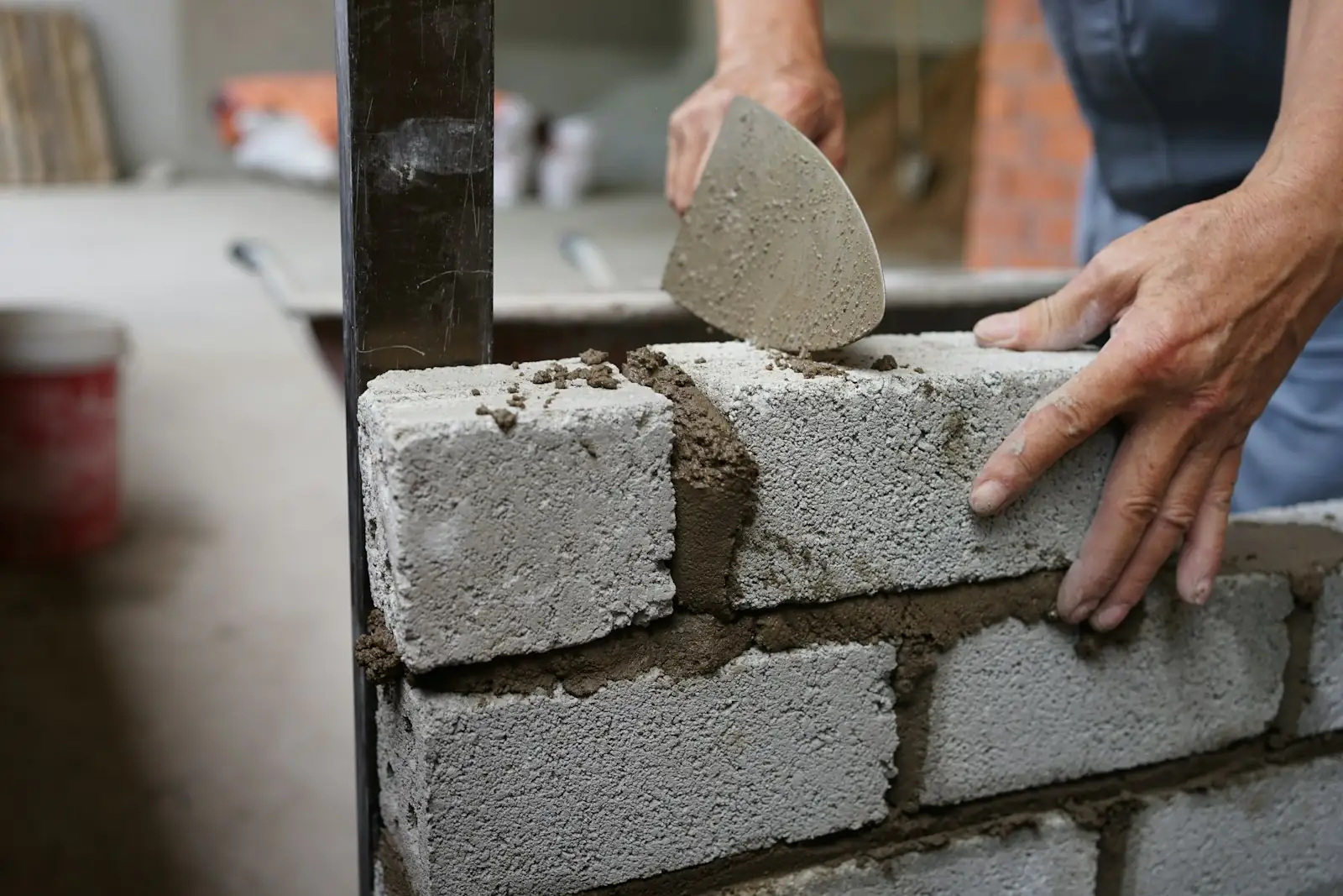 Builder pressing a concrete block into fresh mortar with a trowel