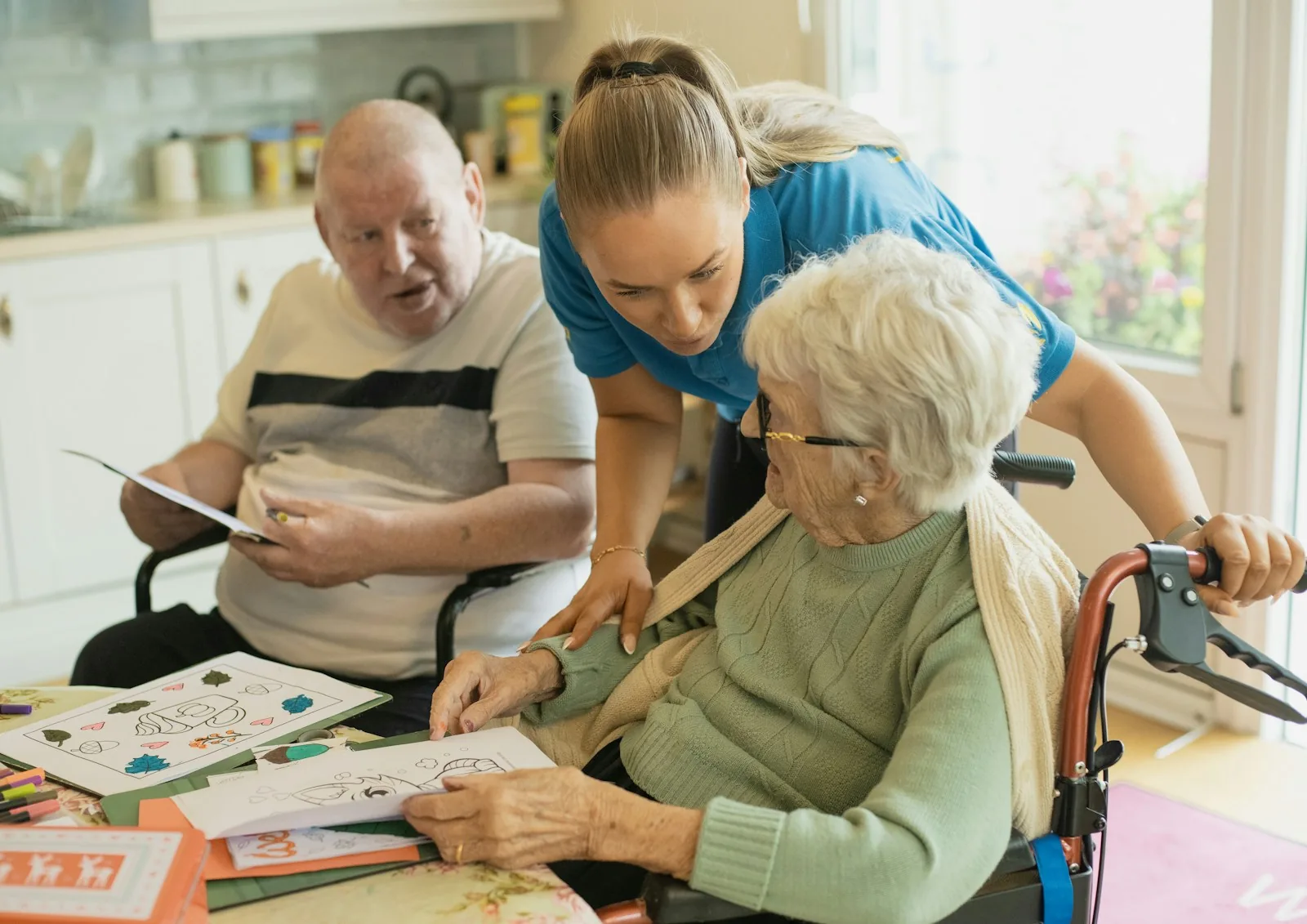 Carer helping an older man and woman with a colouring activity at a table