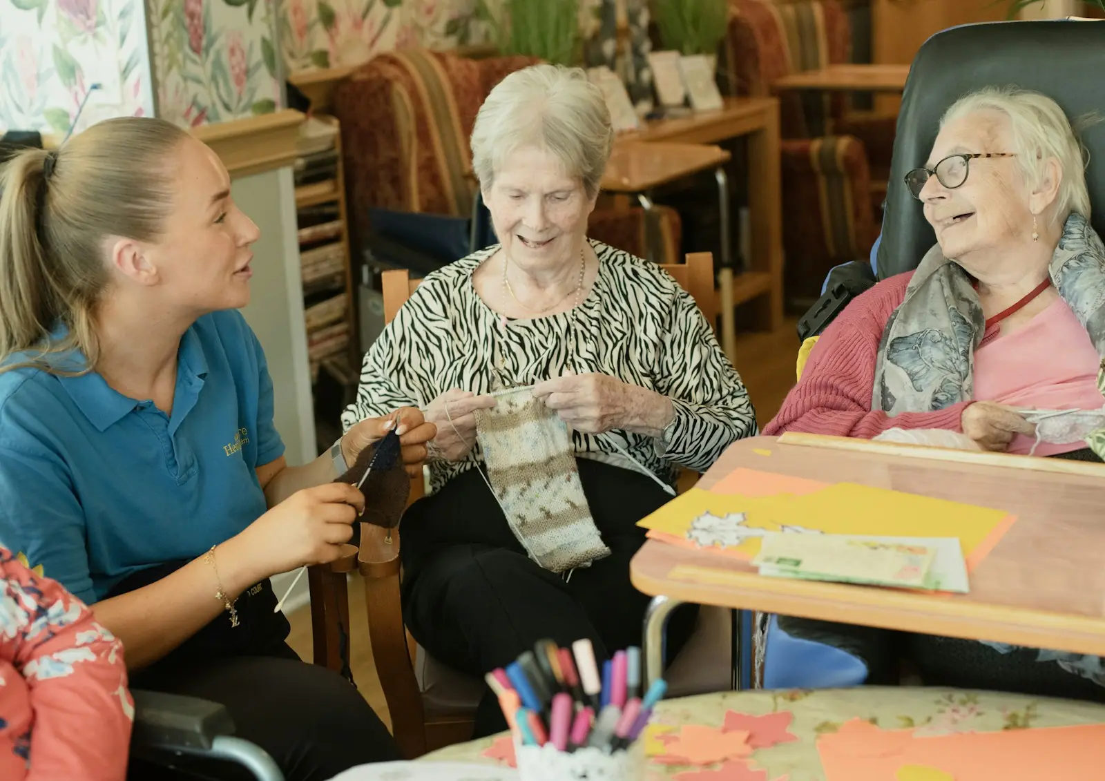 Carer chatting with two older women who are knitting together in a day room