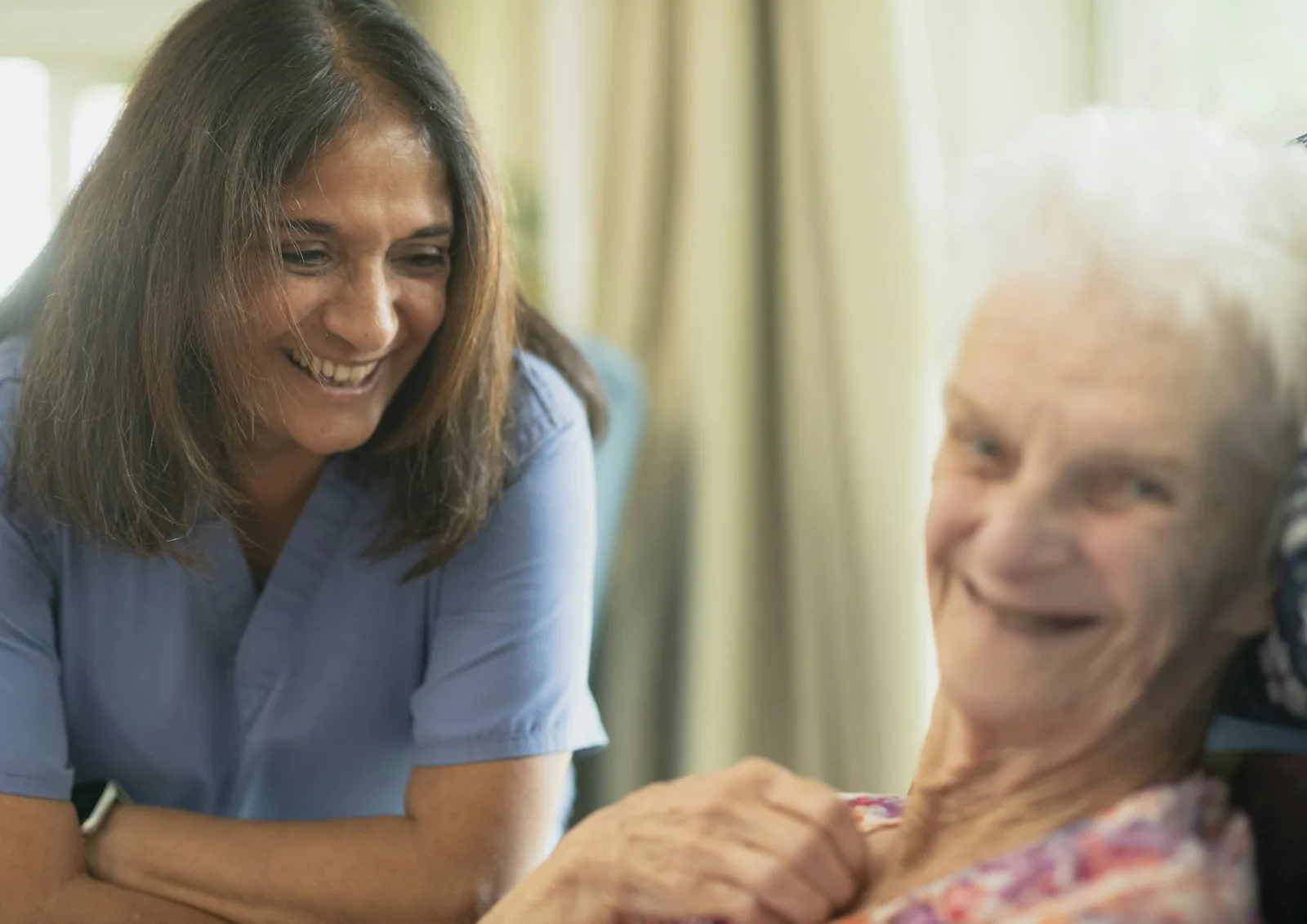 Carer and an older woman laughing together while holding hands