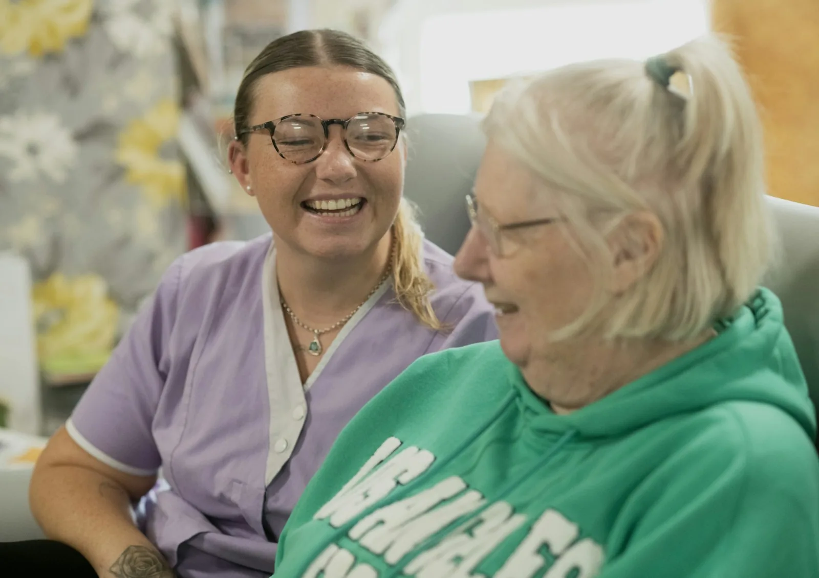 Young carer in a lilac uniform laughing with an older woman