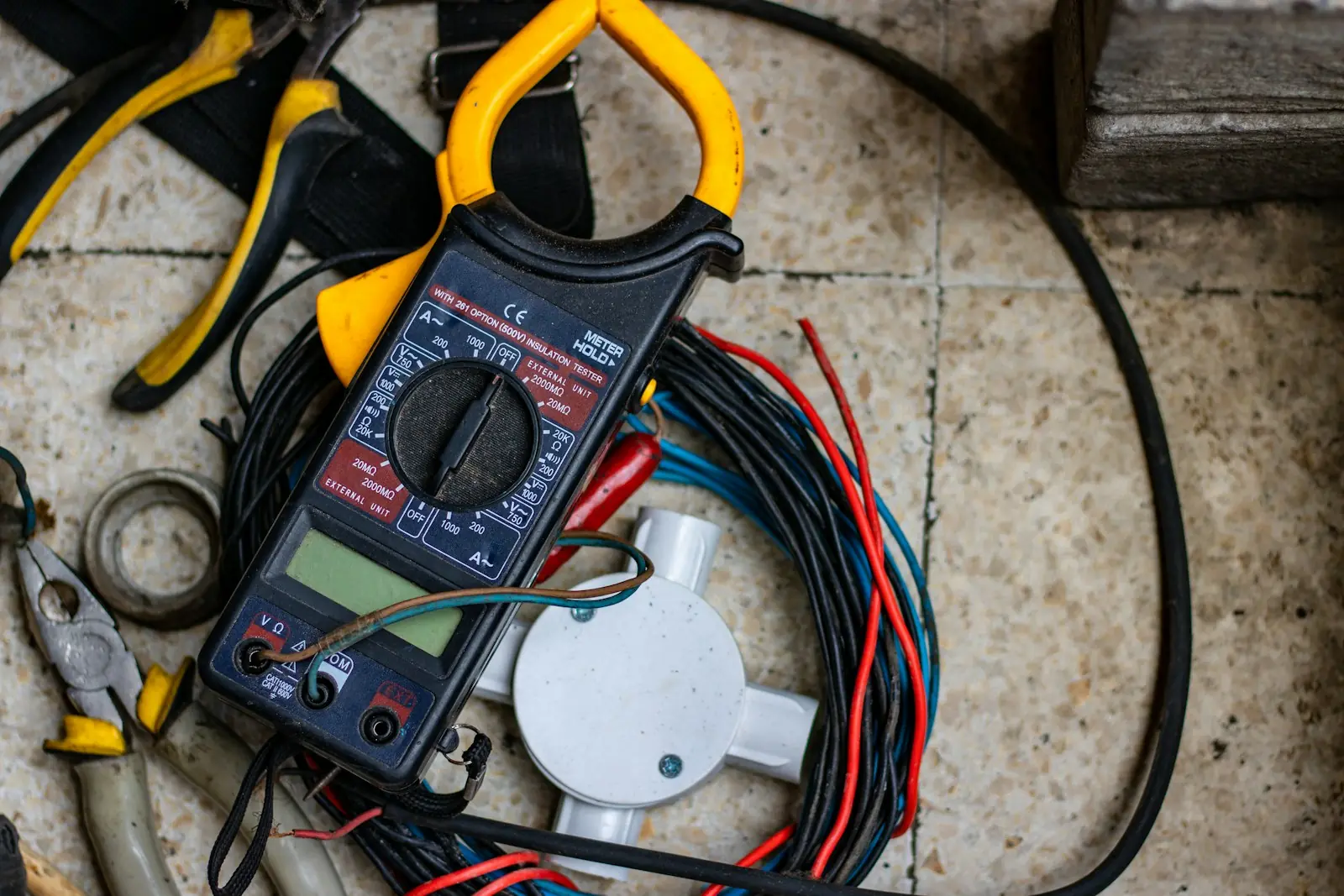 Clamp meter, pliers and coils of cable laid out on a tiled floor