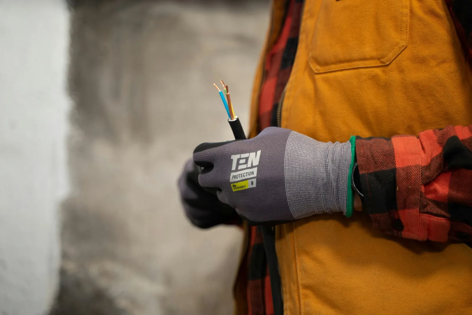 Gloved hand holding a cable with its brown and blue cores stripped