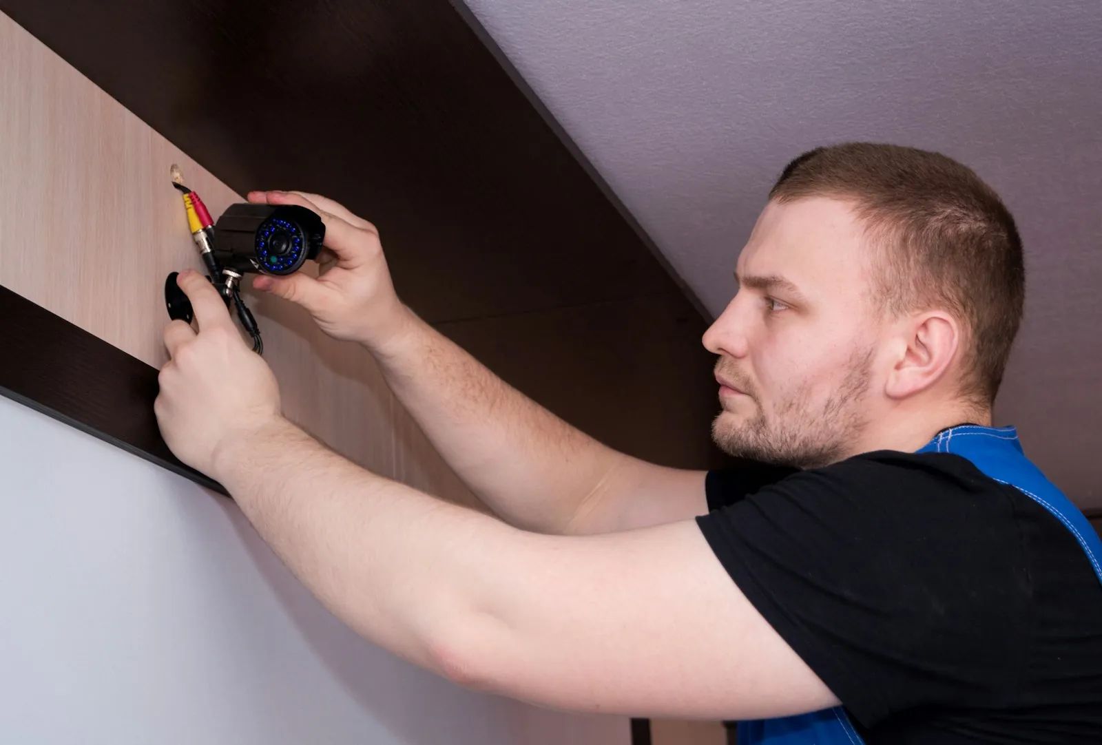 Electrician fitting a security camera to a wall bracket indoors