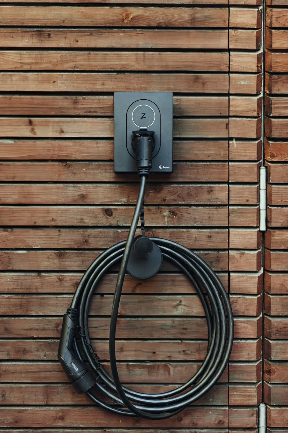 Home electric car charger mounted on a timber-clad wall with its cable coiled below