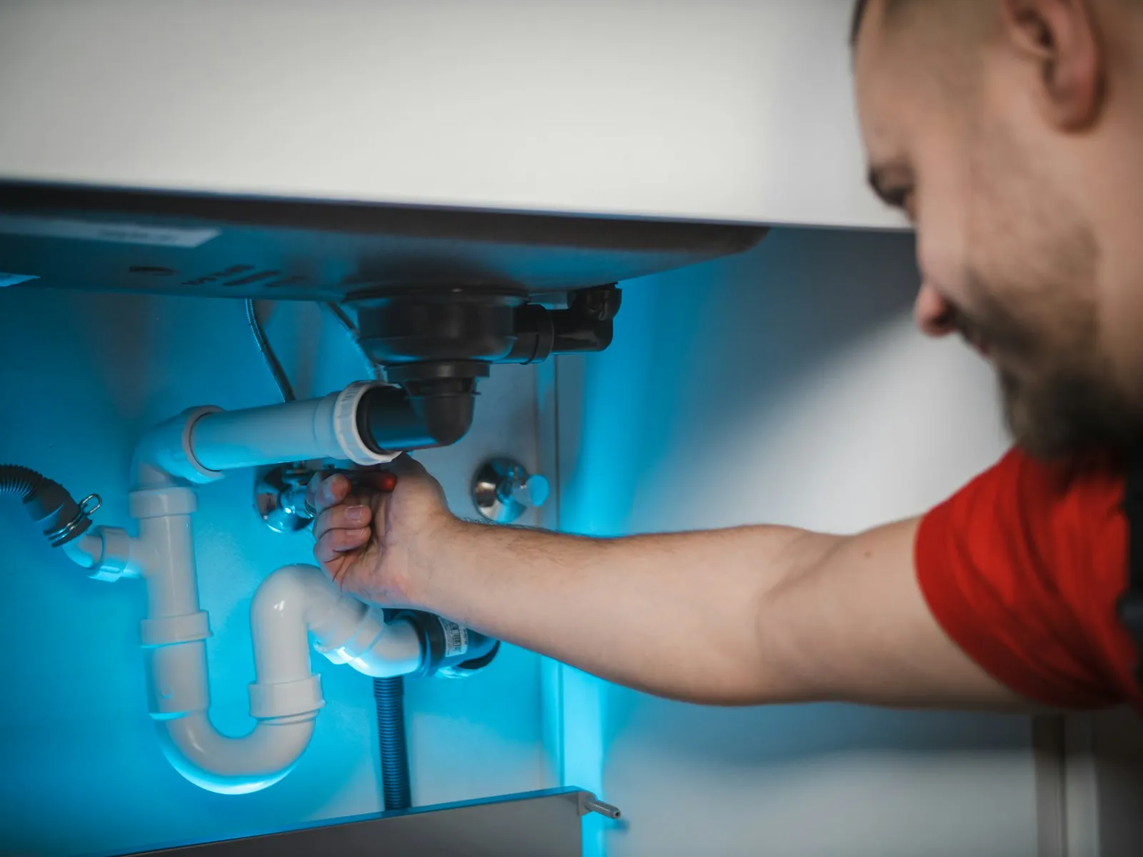 Plumber tightening a waste pipe fitting under a kitchen sink
