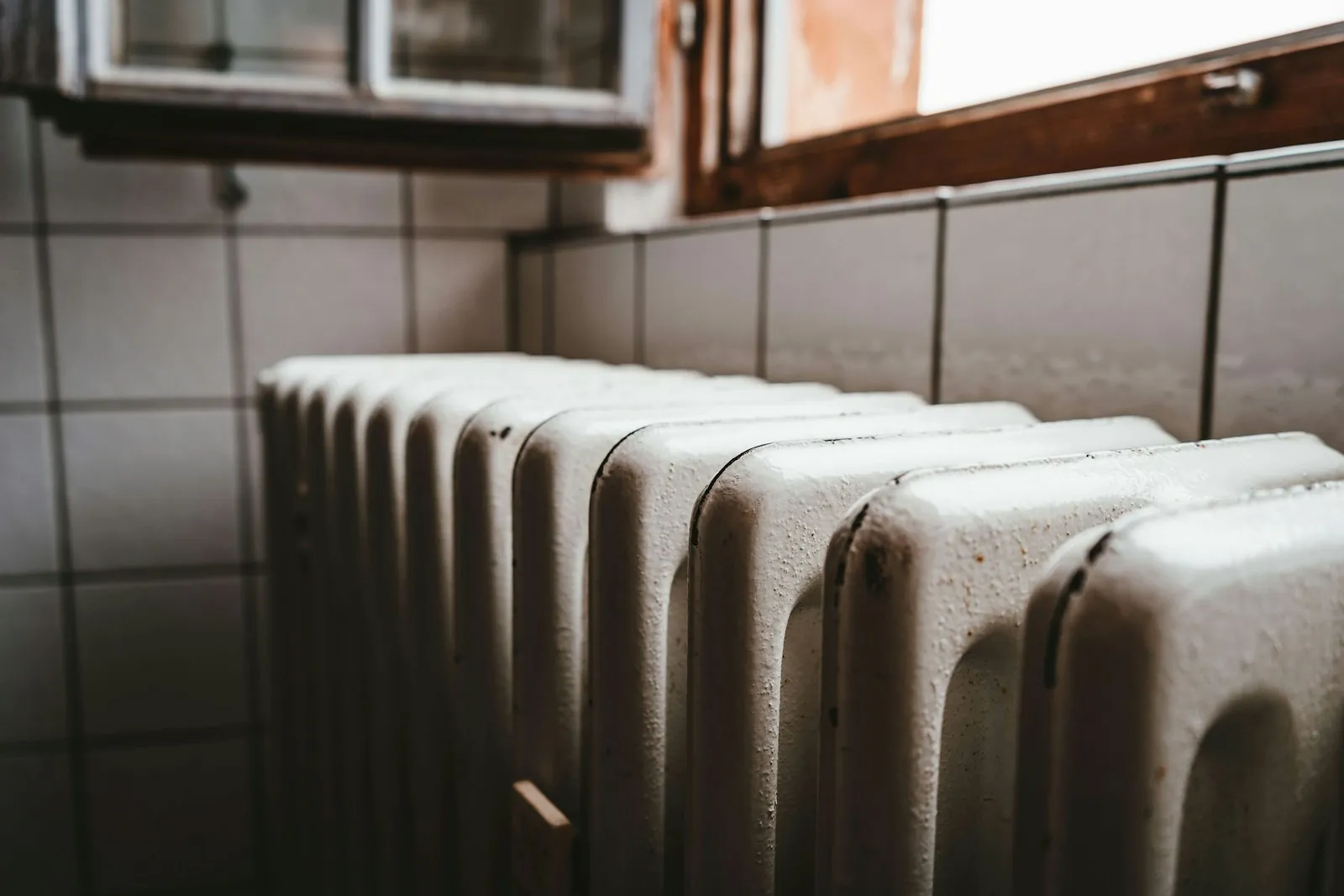 Traditional white column radiator beneath a window in a tiled room