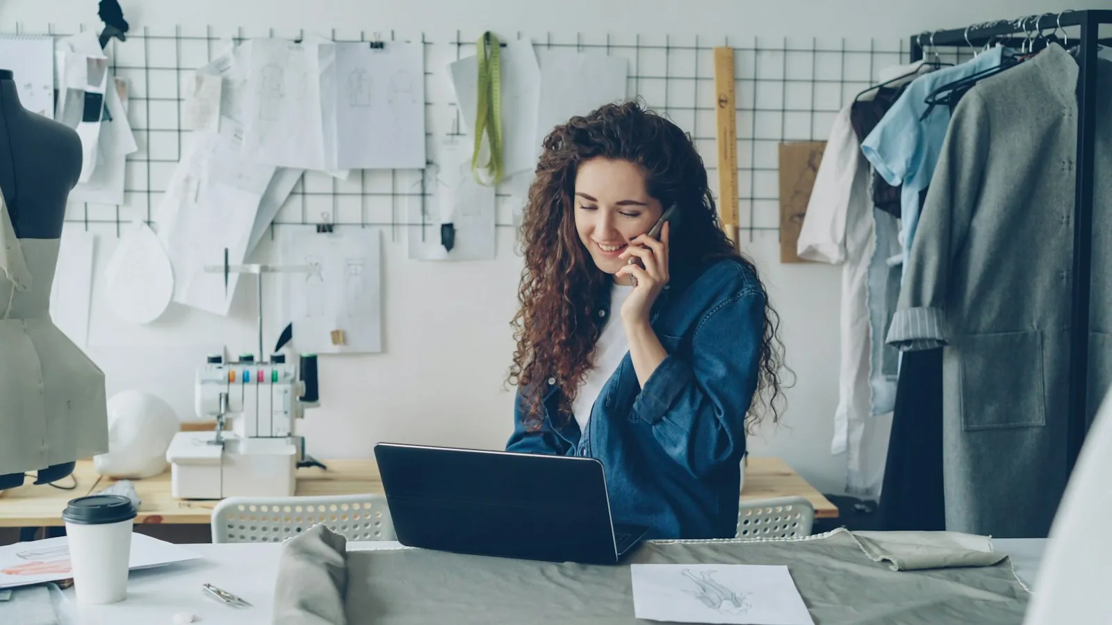 Small business owner smiling on the phone at her studio desk with a laptop open